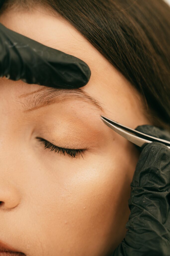 Technicienne en beauté effectuant un soin des sourcils avec une pince à épiler sur le visage d'une cliente