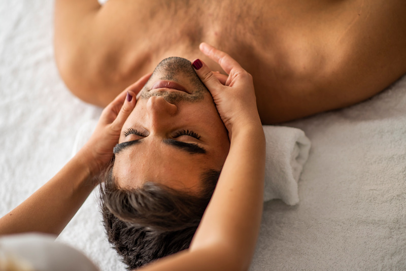 Soin du visage pour un homme détendu recevant un massage facial dans un spa éclairé par une lumière douce