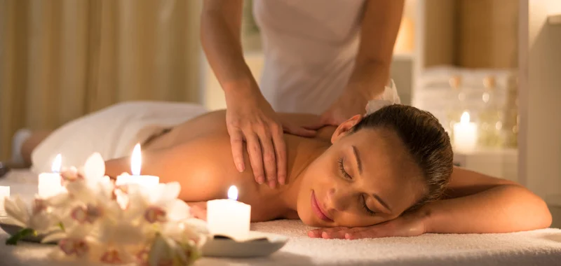 Massage relaxant du dos pour une femme allongée dans un spa avec des bougies et des orchidée