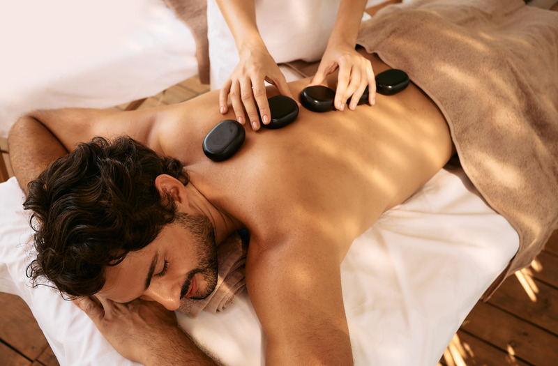 Massage aux pierres chaudes pour un homme détendu dans un spa, avec des pierres de basalte alignées le long de la colonne vertébrale